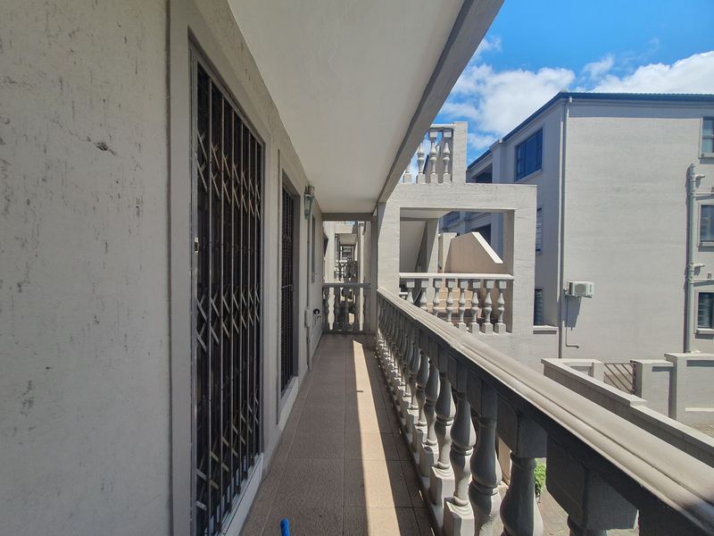 A covered apartment balcony featuring a classic balustrade, tiled flooring, and security gates, offering an outdoor space for relaxation.