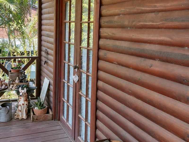A covered timber balcony featuring log-style wall cladding and timber-framed glass french doors, providing a rustic outdoor transition space.