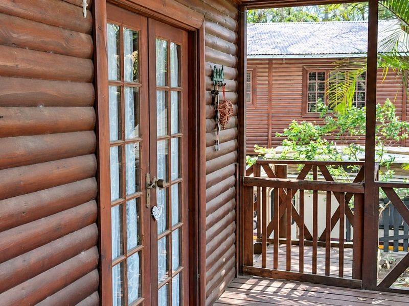 A covered timber balcony featuring log wall cladding, french doors, and a wooden balustrade, offering a rustic outdoor living space.