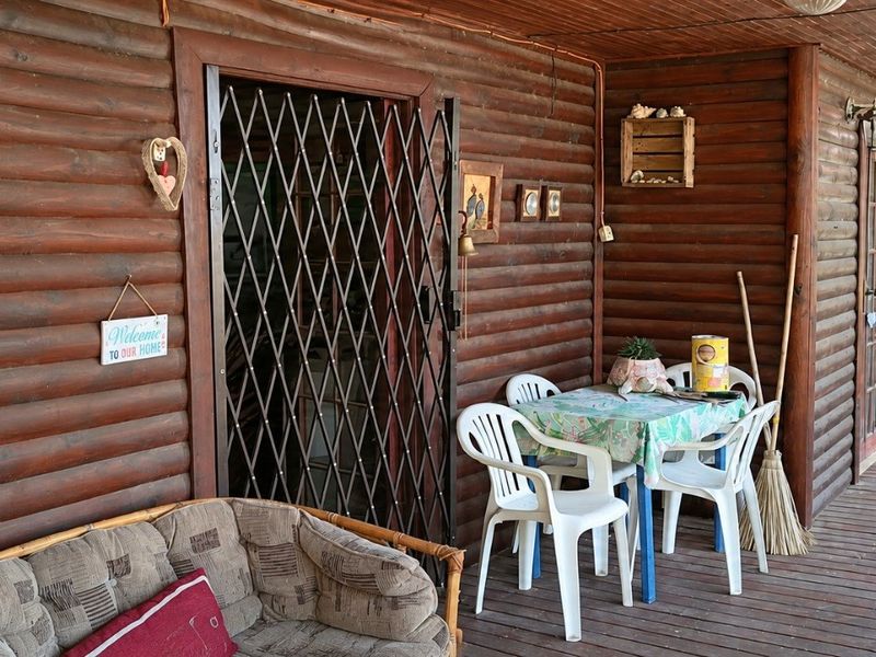 Covered timber patio featuring log wall cladding and wooden decking, providing a rustic outdoor living space.