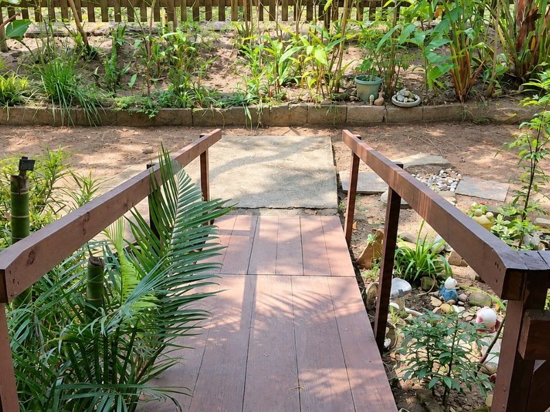 A wooden footbridge leads from the property into a garden area featuring a concrete path and timber fencing.