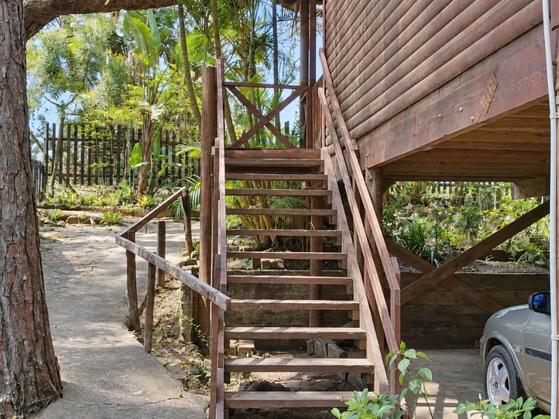 Rear exterior view of a timber townhouse featuring an elevated wooden staircase, paved garden pathway, and natural landscaping.