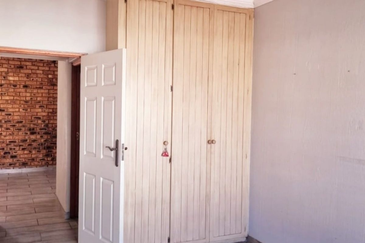 A bedroom featuring built-in wooden cabinetry, tiled flooring, and a classic chandelier, with an adjacent room visible through the doorway.