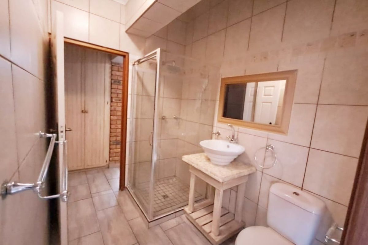 A functional bathroom featuring a glass-enclosed shower, pedestal-style vanity with a vessel sink, and a standard toilet, finished with neutral wall and floor tiles.
