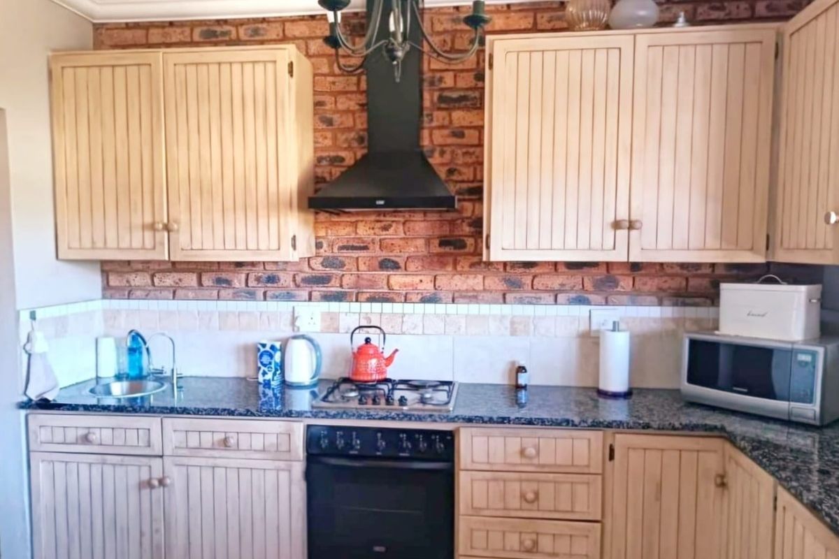 A rustic-style kitchen featuring exposed brick backsplash, granite countertops, wooden cabinetry, and a built-in oven with a black extractor fan.