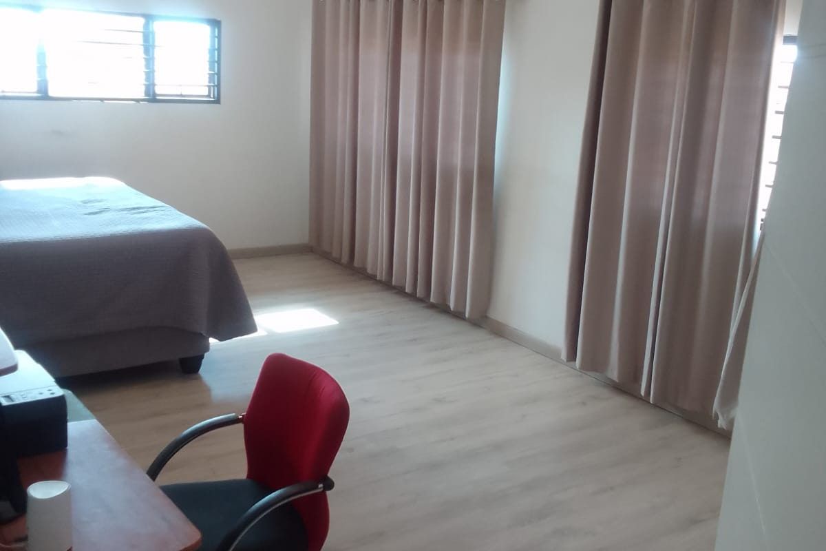 Spacious bedroom featuring light-toned laminate flooring, recessed downlighting, and large windows fitted with security bars.