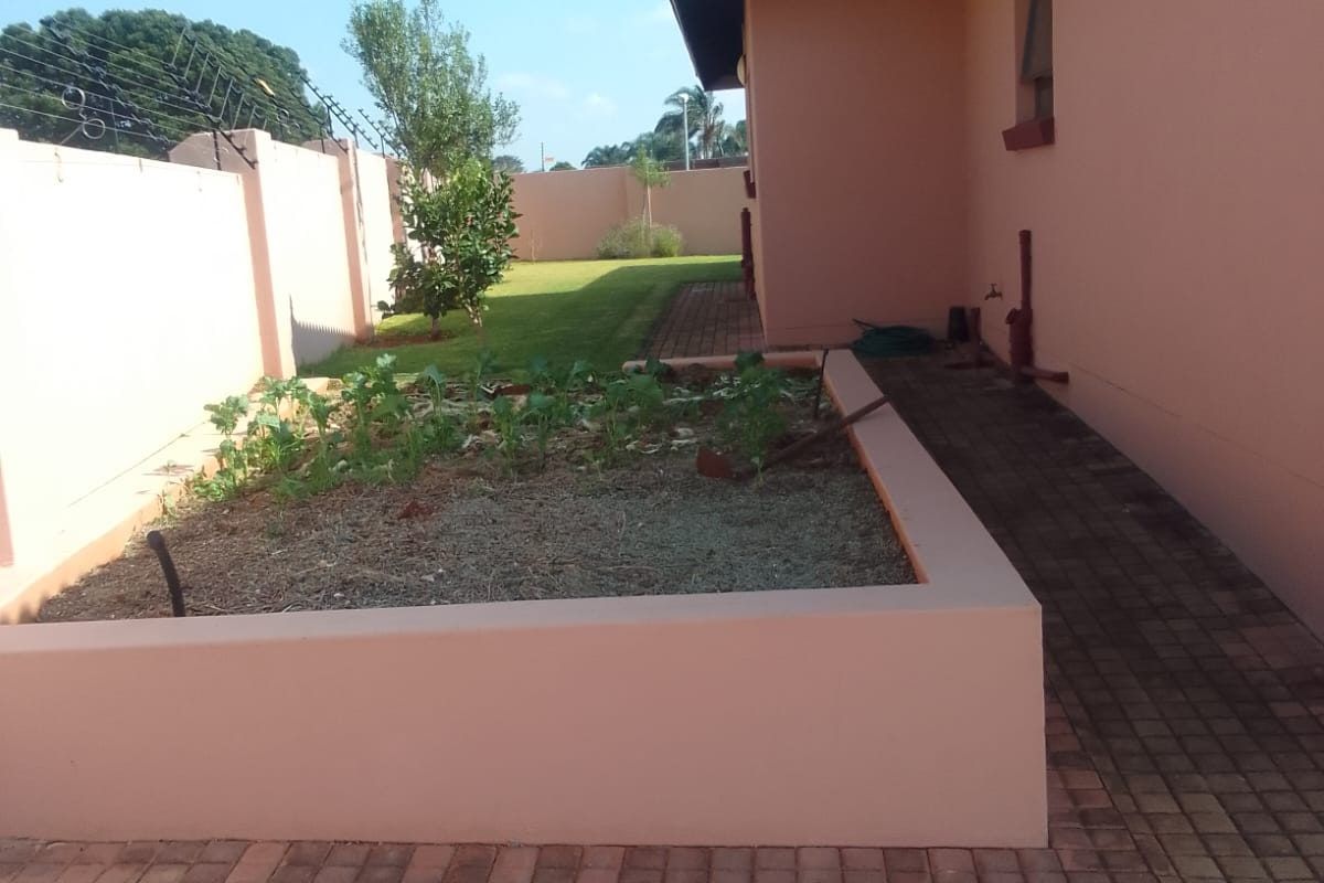 A view of the rear exterior featuring a paved walkway, a raised garden bed, and a perimeter wall with electric fencing.