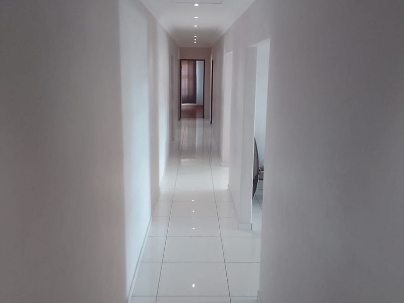 A clean, well-lit hallway featuring modern white floor tiles and recessed ceiling downlights, providing a bright and neutral transition space.