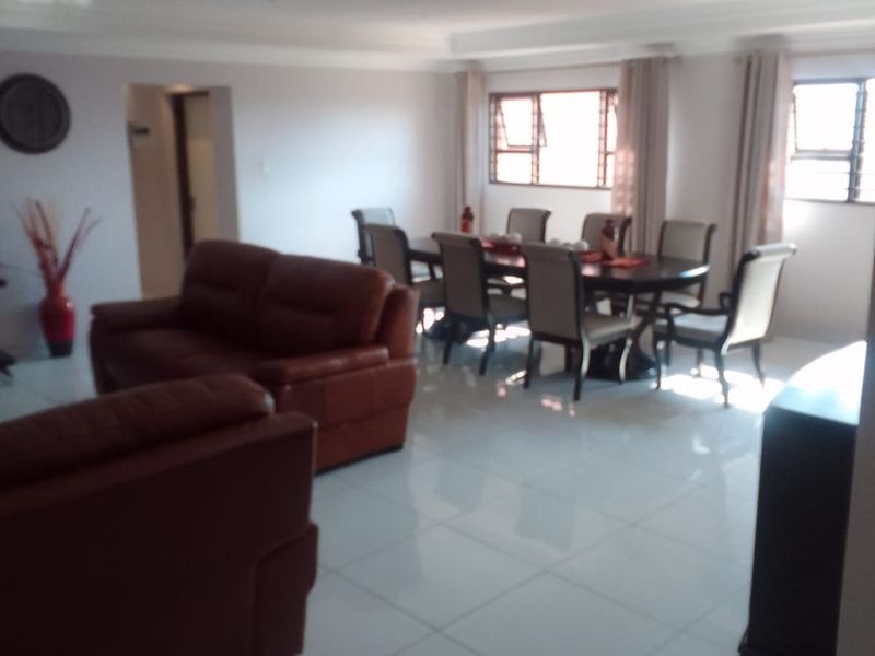 Spacious open-plan living and dining area featuring large windows, bright tiled flooring, and recessed ceiling lighting.