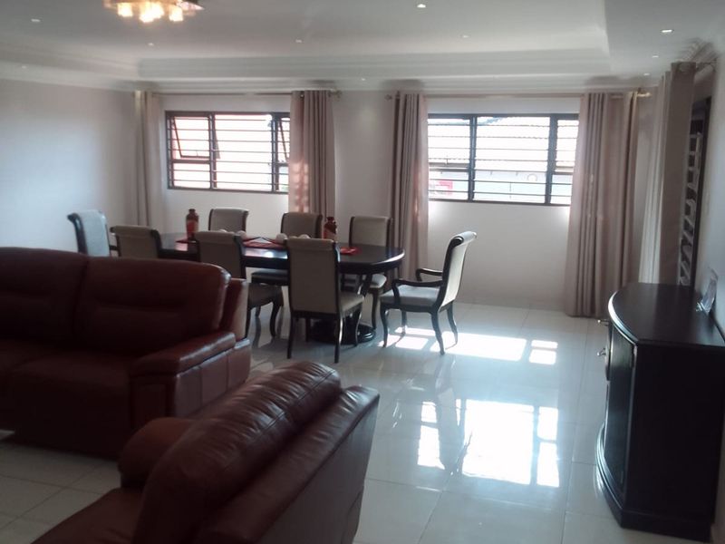 Spacious open-plan living and dining area featuring polished tiled flooring, recessed ceiling lighting, and large windows with security bars.