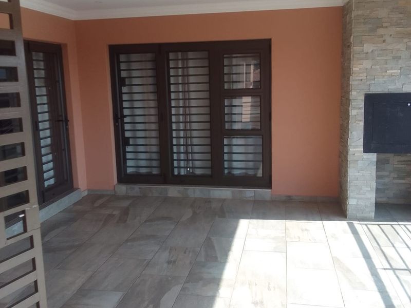 A covered patio area featuring tiled flooring, a built-in fireplace with stone cladding, and secure access doors.
