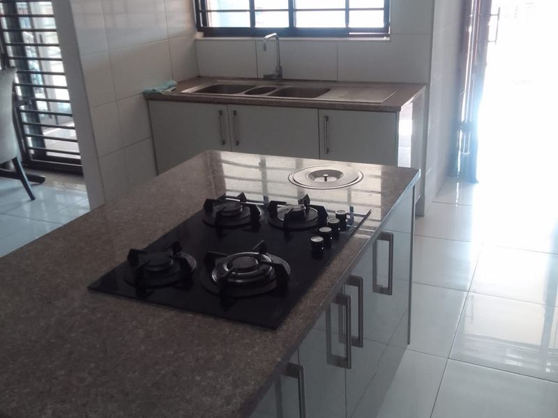Modern kitchen featuring a central island with a built-in gas cooktop, extractor fan, double sink, and tiled finishes throughout.