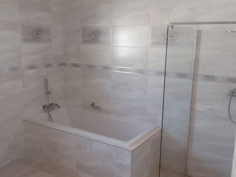 Modern bathroom featuring a built-in bathtub, a separate walk-in shower with a glass screen, and neutral wall and floor tiling.
