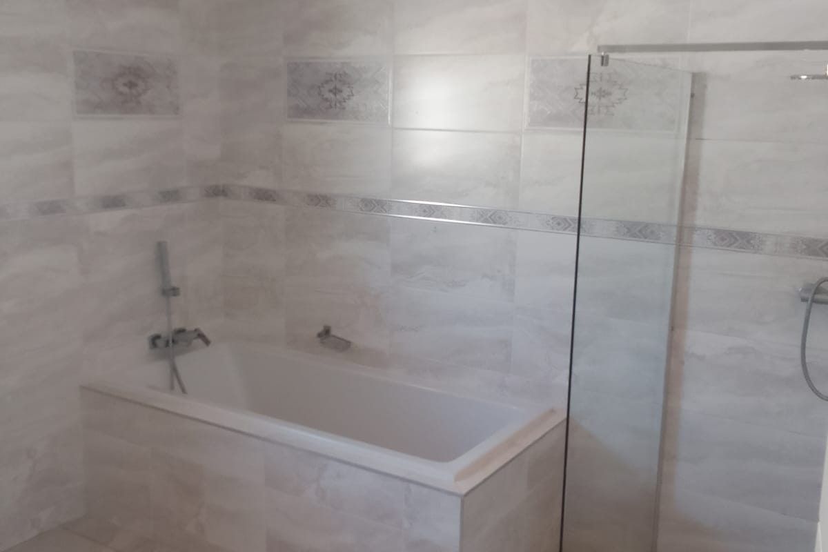 Modern bathroom featuring a built-in bathtub, a separate walk-in shower with a glass screen, and neutral wall and floor tiling.