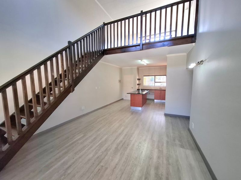 Spacious open-plan living area featuring a timber staircase leading to a mezzanine level, complemented by a functional kitchen with island and modern laminate flooring.