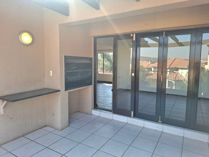 Covered balcony featuring a built-in braai, stone prep counter, tiled flooring, and folding glass doors providing access to the interior living space.
