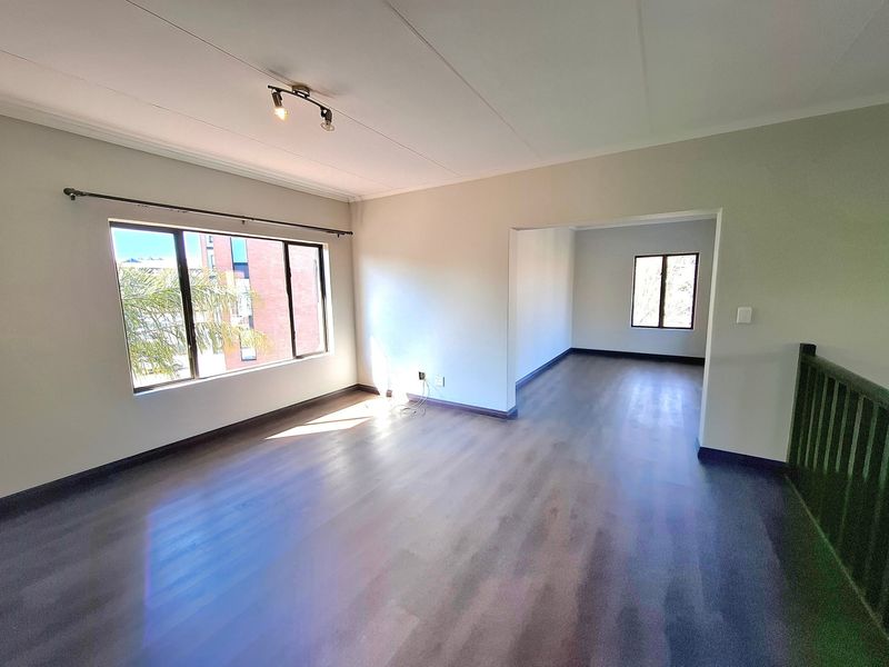 A bright and spacious open-plan living area featuring modern laminate flooring, neutral walls, and a staircase balustrade, offering a versatile layout.
