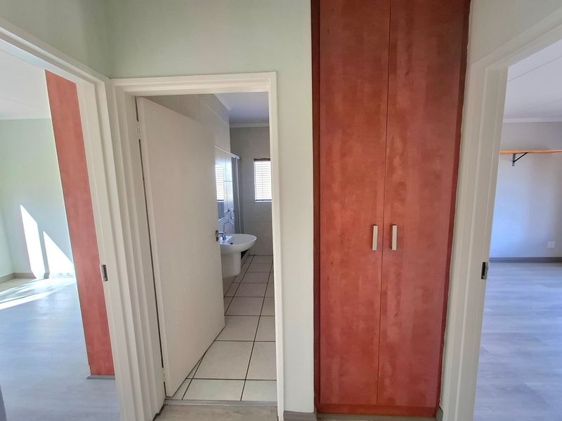 A bright hallway featuring built-in wooden cabinetry and direct access to an adjacent bathroom with tiled flooring and a pedestal basin.