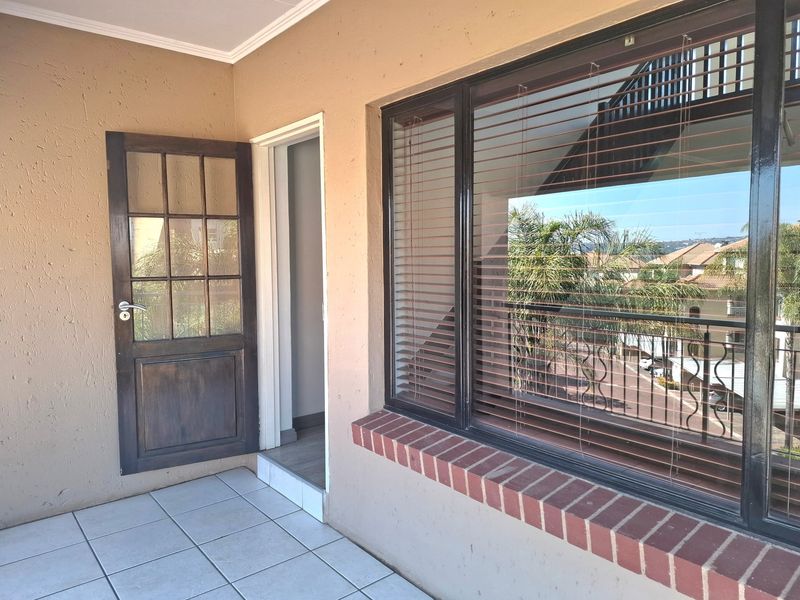 A clean, tiled balcony area featuring a timber-framed glass door and a large window with a brick sill and venetian blinds.