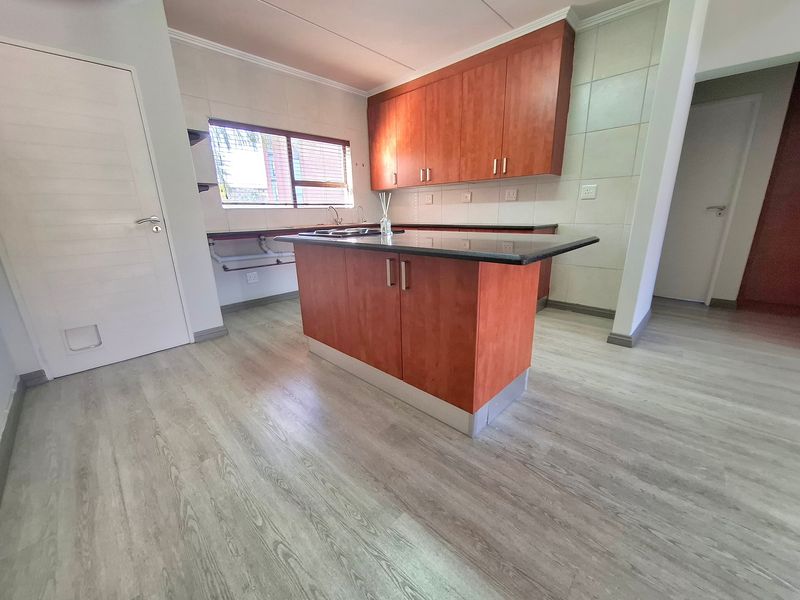 A clean, functional kitchen featuring a central island with granite countertops, wood-finish cabinetry, and light-toned laminate flooring.