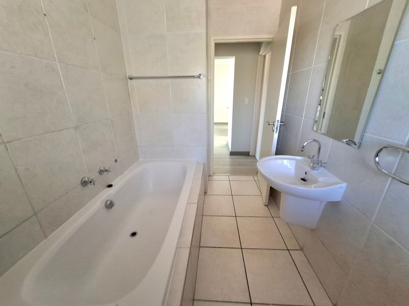 A functional bathroom featuring a bathtub, pedestal basin, and neutral wall and floor tiling, providing a clean and practical space.
