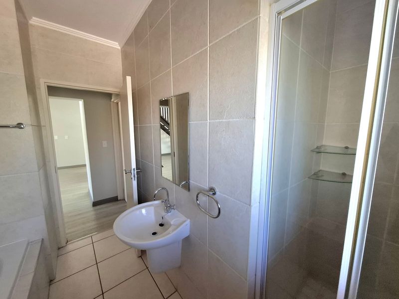 A clean, neutral-toned bathroom featuring a pedestal washbasin, a glass-enclosed shower, and modern ceramic tiling throughout.