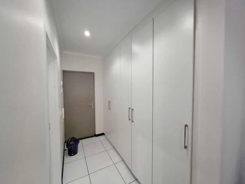 A clean, well-maintained hallway featuring white tiled flooring and extensive built-in storage cupboards with modern handles.