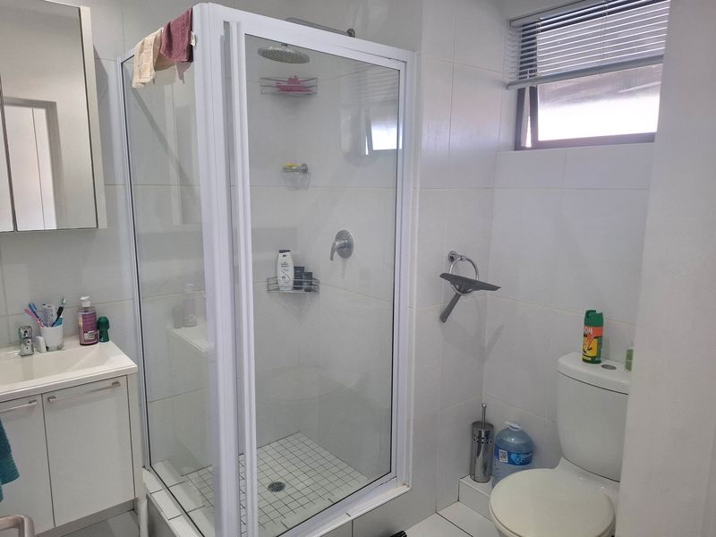 A clean, functional bathroom featuring a glass-enclosed shower, vanity unit with basin, and a standard toilet with white wall tiling.