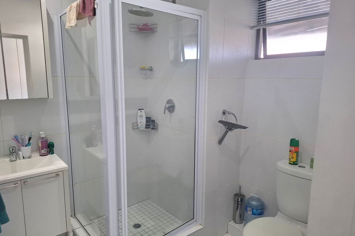 A clean, functional bathroom featuring a glass-enclosed shower, vanity unit with basin, and a standard toilet with white wall tiling.