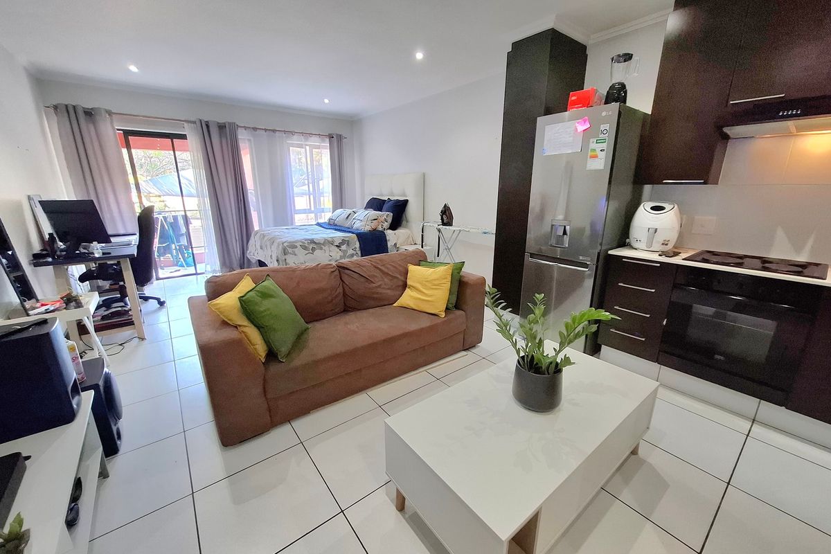 Open-plan studio apartment featuring a modern kitchen with dark cabinetry, tiled flooring, and direct access to a balcony through sliding glass doors.