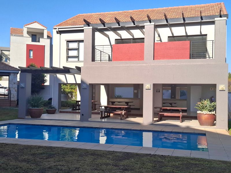 A well-maintained communal pool area featuring a covered patio with a pergola, tiled flooring, and an adjacent balcony.