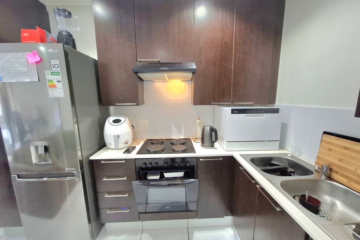 Compact kitchen featuring dark wood cabinetry, electric hob with extractor fan, built-in oven, and a double stainless steel sink with tiled backsplash.