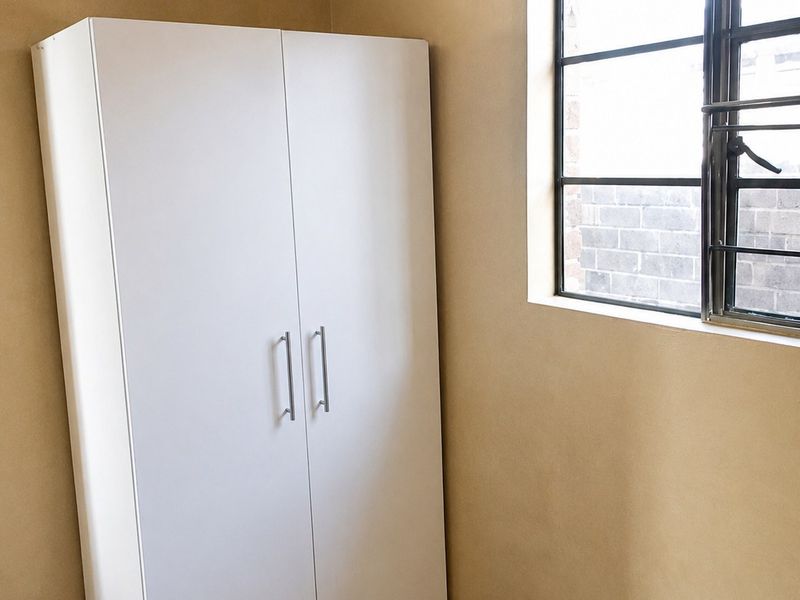 A simple bedroom featuring tiled flooring, neutral wall finishes, and a window fitted with security bars.