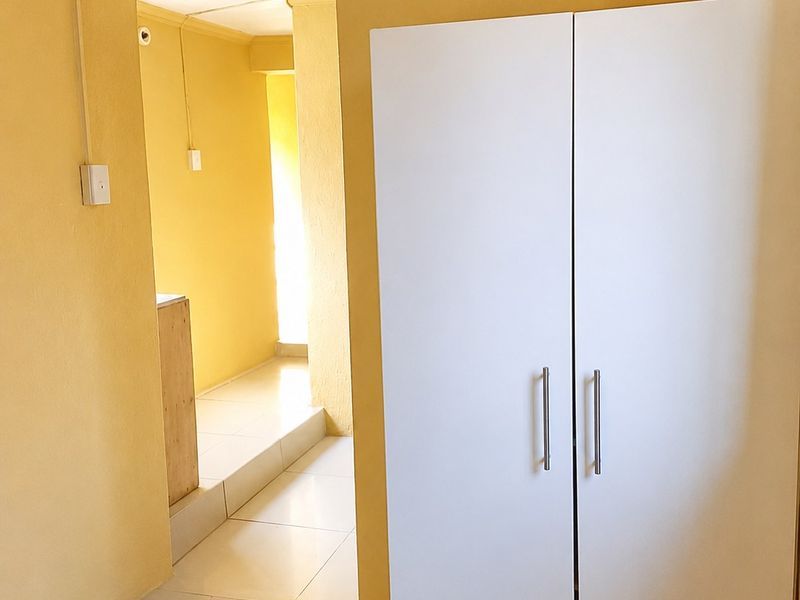A hallway area featuring tiled flooring and a built-in cupboard, leading into an adjacent room with a step-up transition.