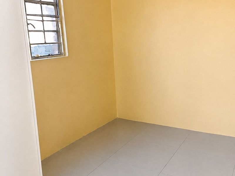 A clean, empty bedroom featuring neutral yellow walls, grey tiled flooring, and a window fitted with security bars.