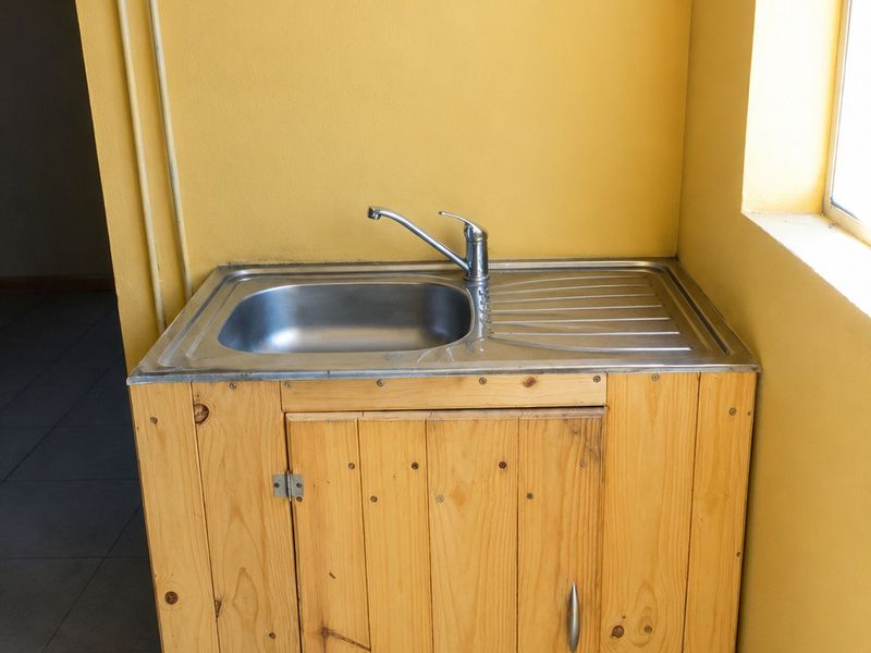A basic utility area featuring a stainless steel sink set into a custom-built wooden cabinet against a yellow wall.