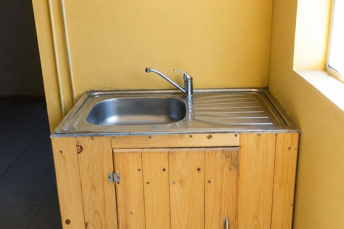 A basic utility area featuring a stainless steel sink set into a custom-built wooden cabinet against a yellow wall.