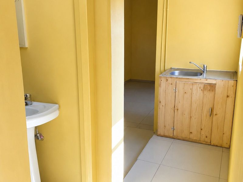 A utility area featuring a pedestal basin and a small kitchenette sink with a wooden vanity cabinet, finished with tiled flooring.
