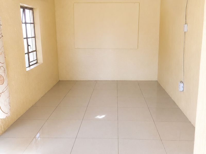 A clean, empty bedroom featuring neutral yellow walls, tiled flooring, and a ceiling fan, offering a blank canvas for personalization.