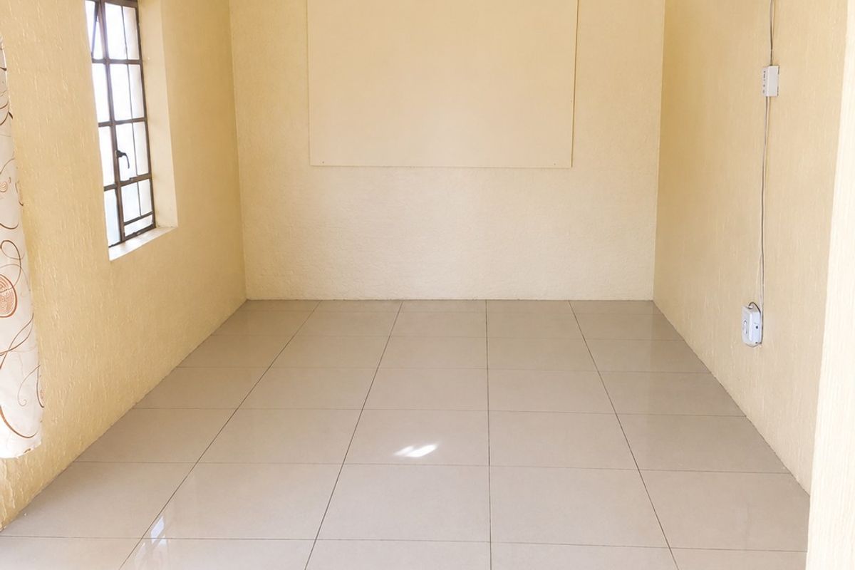A clean, empty bedroom featuring neutral yellow walls, tiled flooring, and a ceiling fan, offering a blank canvas for personalization.