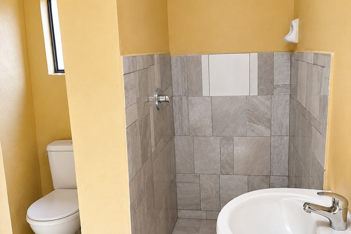 A functional bathroom featuring a pedestal basin, a tiled shower enclosure with a modern shower head, and a standard toilet.