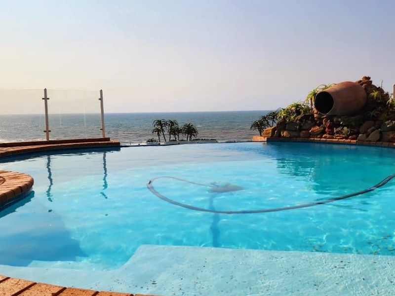 An inviting infinity pool featuring a rock water feature and glass balustrades, offering stunning ocean views.