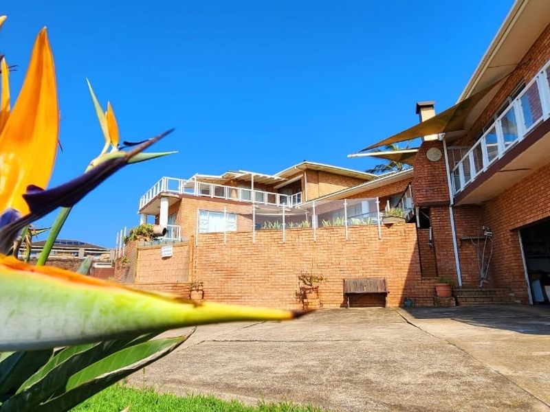 A view of the rear exterior featuring a brick facade, concrete patio area, and glass balustrades leading to an elevated terrace.