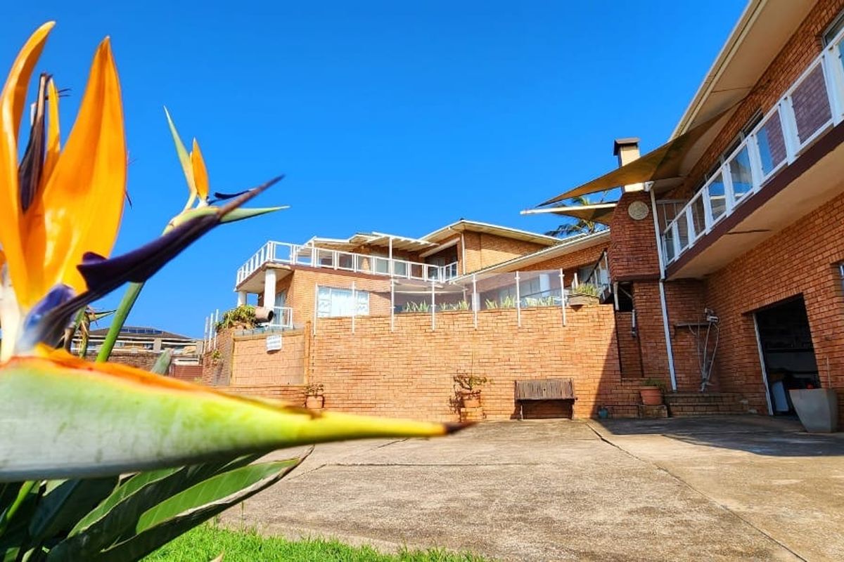 A view of the rear exterior featuring a brick facade, concrete patio area, and glass balustrades leading to an elevated terrace.