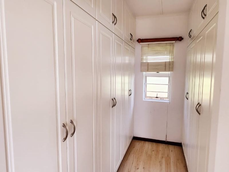 A walk-in dressing area featuring extensive floor-to-ceiling built-in cabinetry, laminate flooring, and a window with a fitted blind.