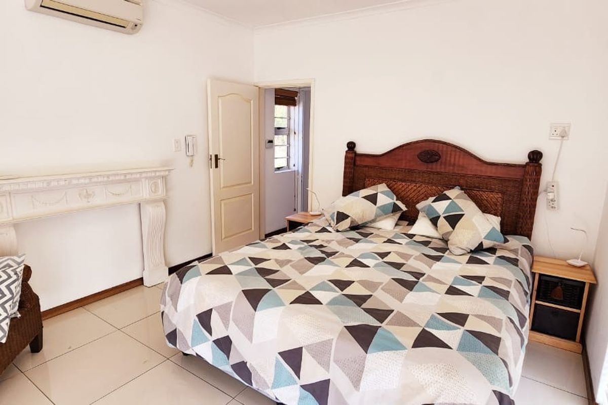 A bedroom featuring tiled flooring, a decorative fireplace mantel, and a wall-mounted air conditioning unit.