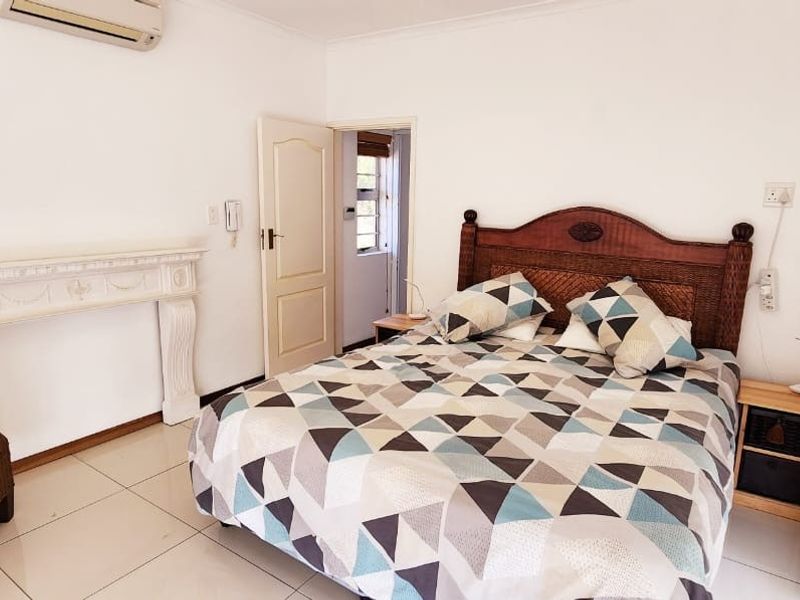 A bedroom featuring tiled flooring, a decorative fireplace mantel, and a wall-mounted air conditioning unit.