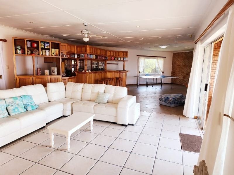 Spacious open-plan living area featuring a built-in wooden bar, tiled flooring, and large sliding glass doors providing natural light and garden access.