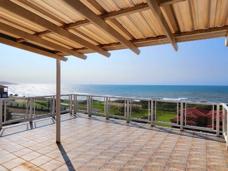 Spacious covered balcony featuring tiled flooring and a glass balustrade, offering expansive, unobstructed ocean views.