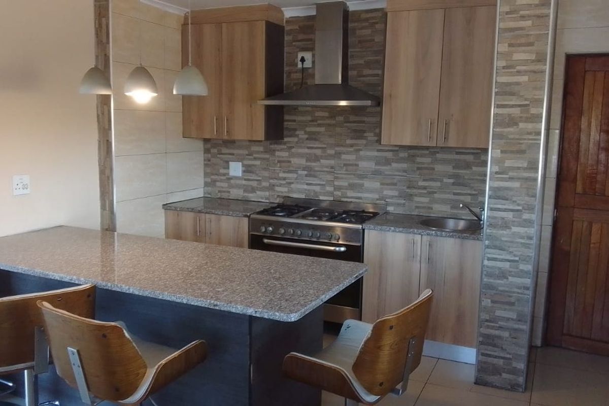 Modern kitchen featuring wood-finish cabinetry, granite countertops, a breakfast bar, and a stainless steel gas stove with an extractor fan.